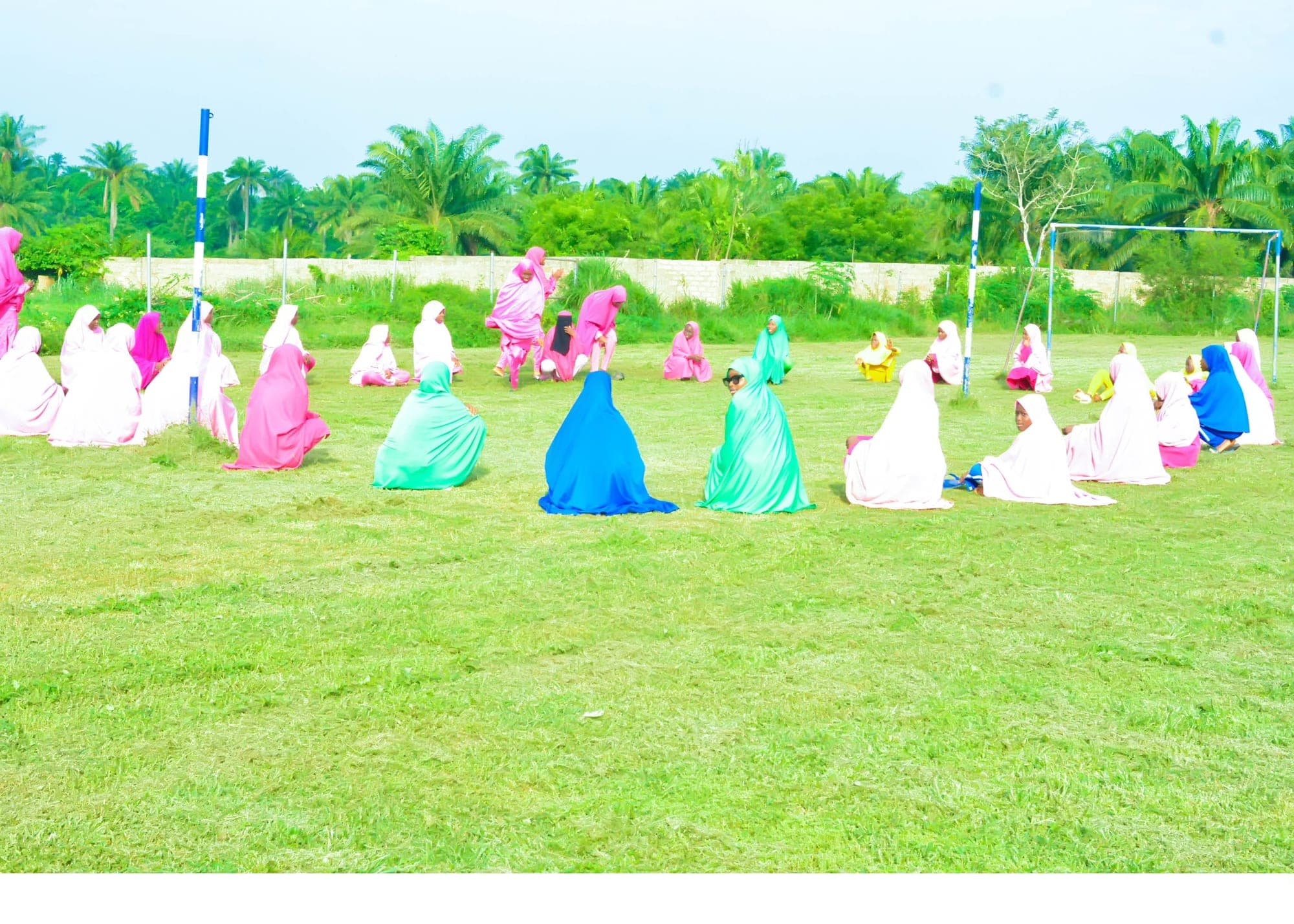 Girls in colourful hijabs seated together on the school field