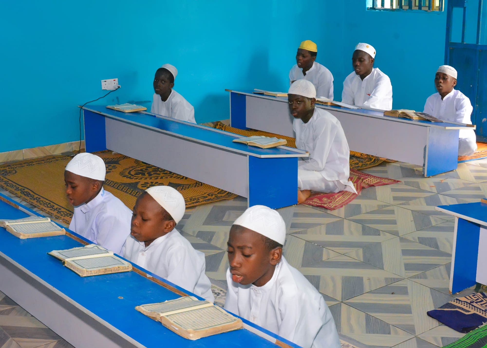 Tahfiz boys in white caps reading the Qur’an at long blue desks