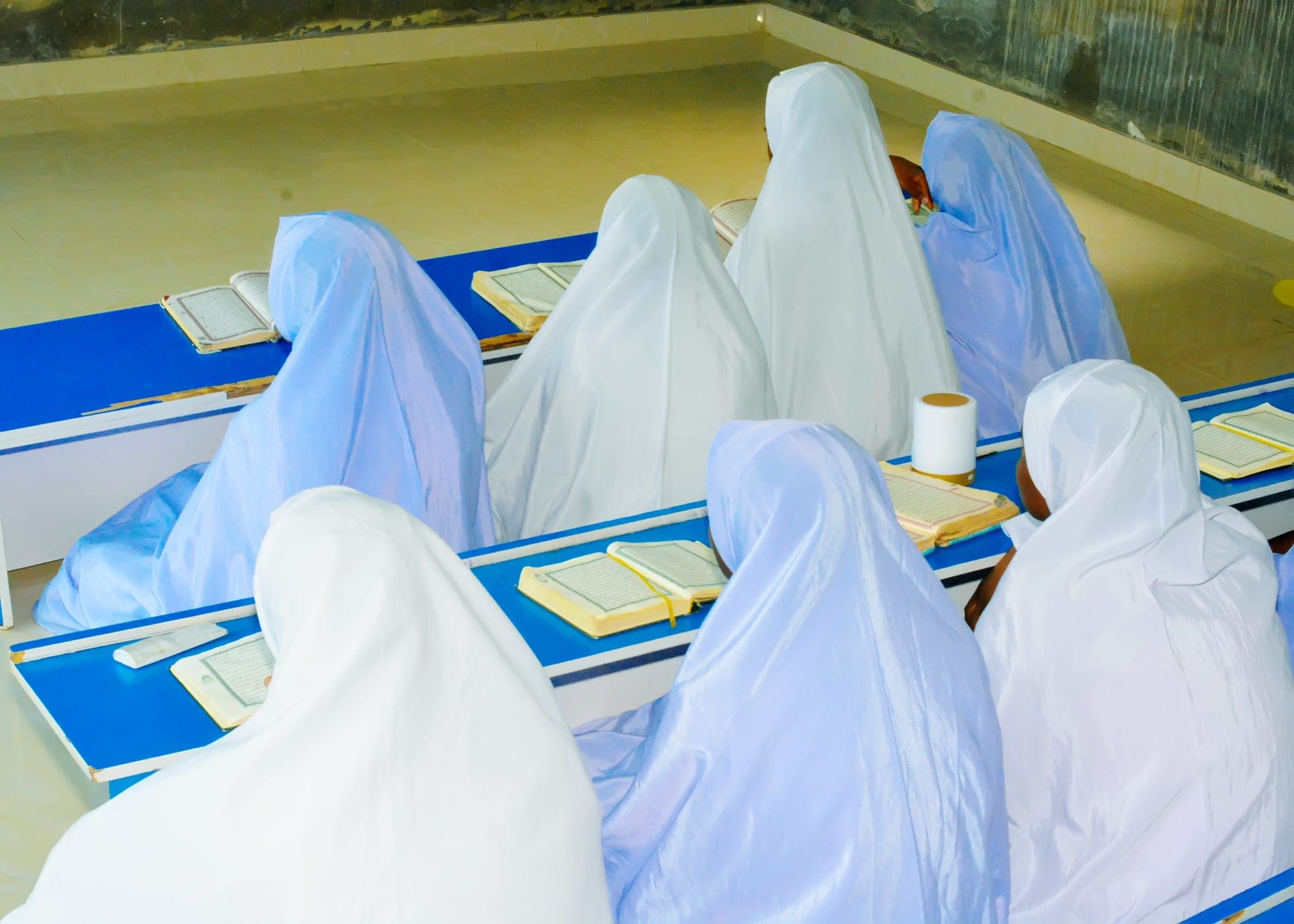 Tahfiz girls gathered around blue desks with their Qur’ans